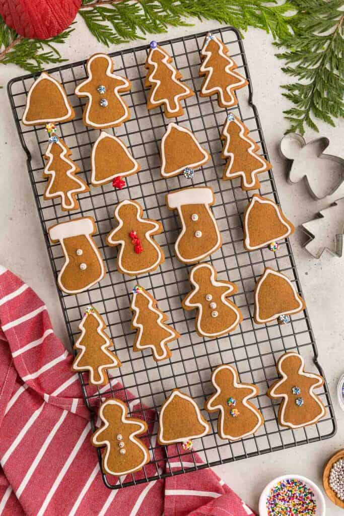 Overhead picture of a cooling rack filled with gingerbread cookies all outlined with white royal icing. Two of the stocking shaped cookies have been flooded with icing, and some of the cookies have sprinkles on them.