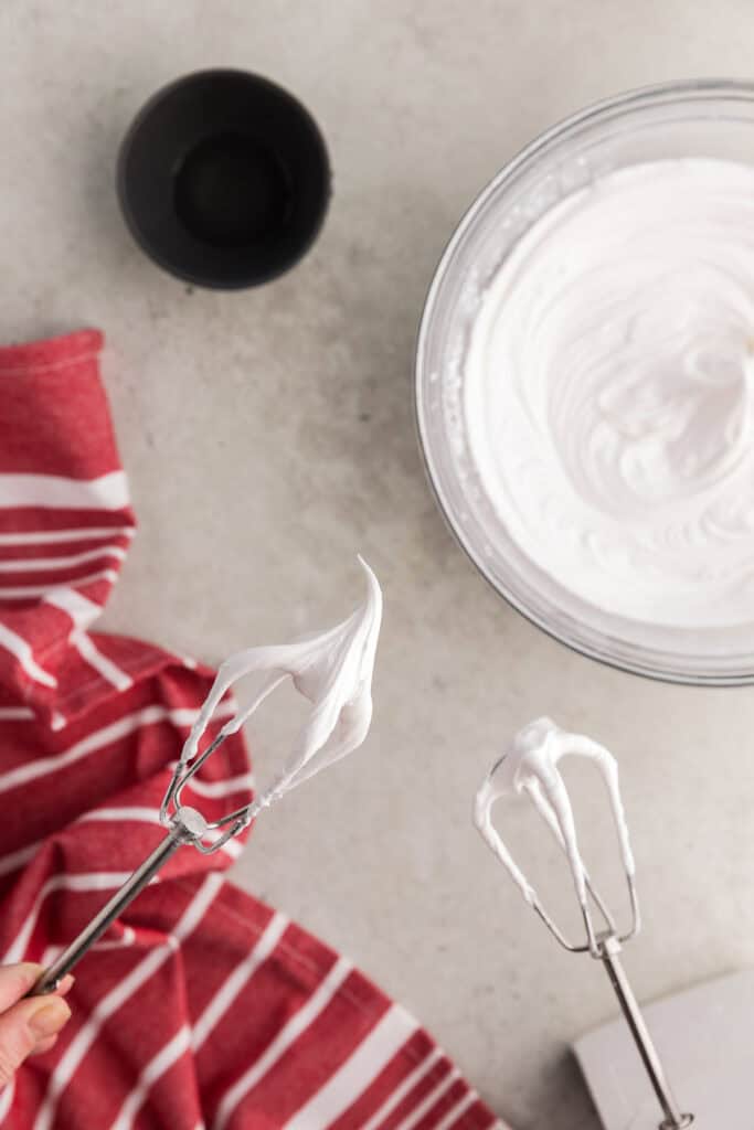 Overhead shot of the beaters pulled out of the whipped royal icing with meringue powder.  The icing is very white and a stiff peak can be seen poking up from the beater.
