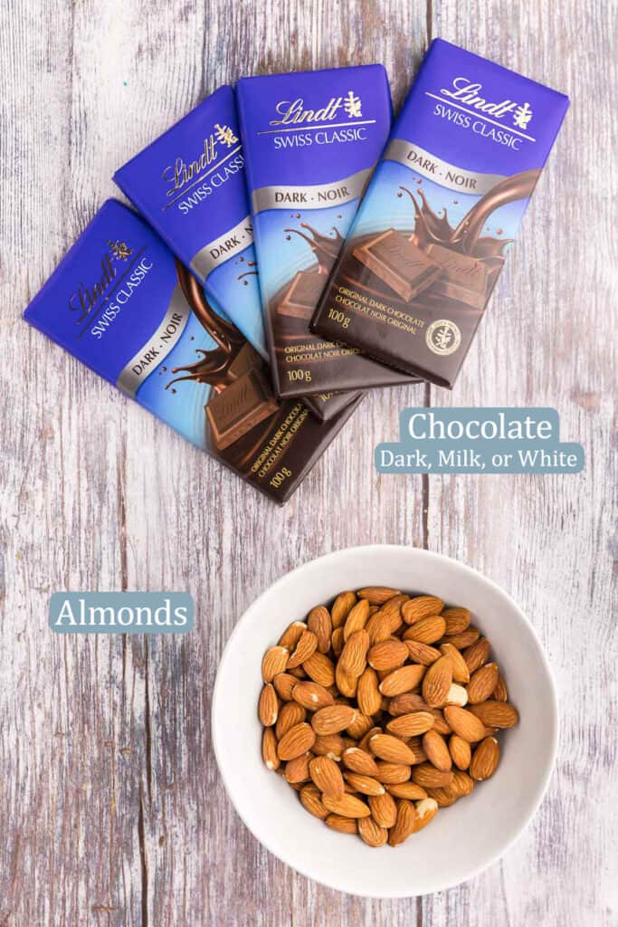 Overhead shot of the ingredients needed to make almond bark.  Ingredients include your choice of chocolate (dark, milk or white), and raw almonds.  I have shown 4 dark chocolate Lindt bars.