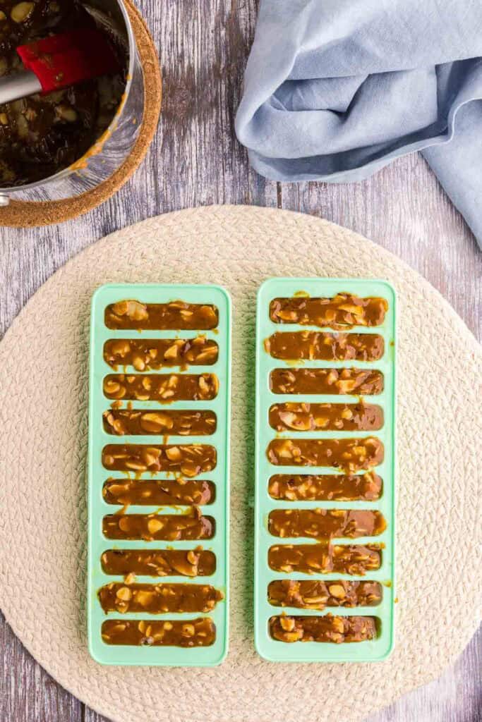 Overhead shot of the hot toffee mixture after it has been poured into silicone molds with log shapes. There are two green silicone molds filled to the top cleanly with the toffee.
