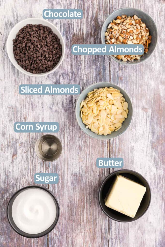 Overhead shot of the ingredients needed to make Buttercrunch. Ingredients are: chocolate chips, chopped almonds, sliced almonds, granulated white sugar, salted butter, and corn syrup.