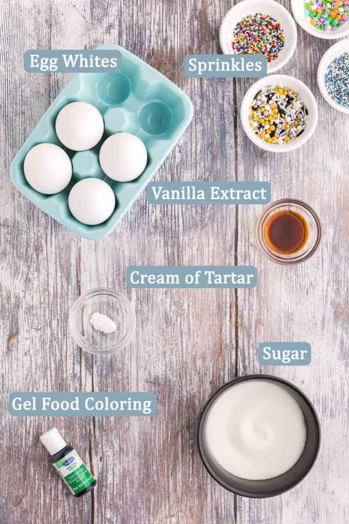 Overhead shot of the ingredients needed to make Christmas Tree Meringues.  Ingredients include: Egg whites, sprinkles, vanilla extract, cream of tartar, sugar, and gel food coloring (green).