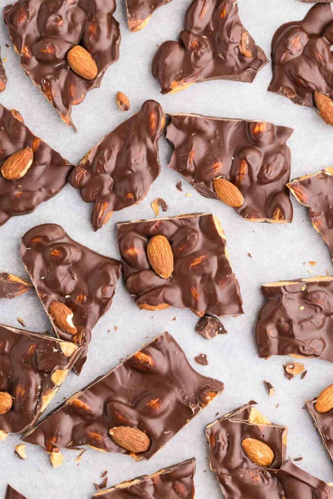 Close up overhead shot of dark chocolate almond bark after it has been broken into pieces about 2" by 2".  Some almonds are just lumps under chocolate while other almonds are fully visible on top.  Almond bark milk chocolate can also be made by using milk chocolate.