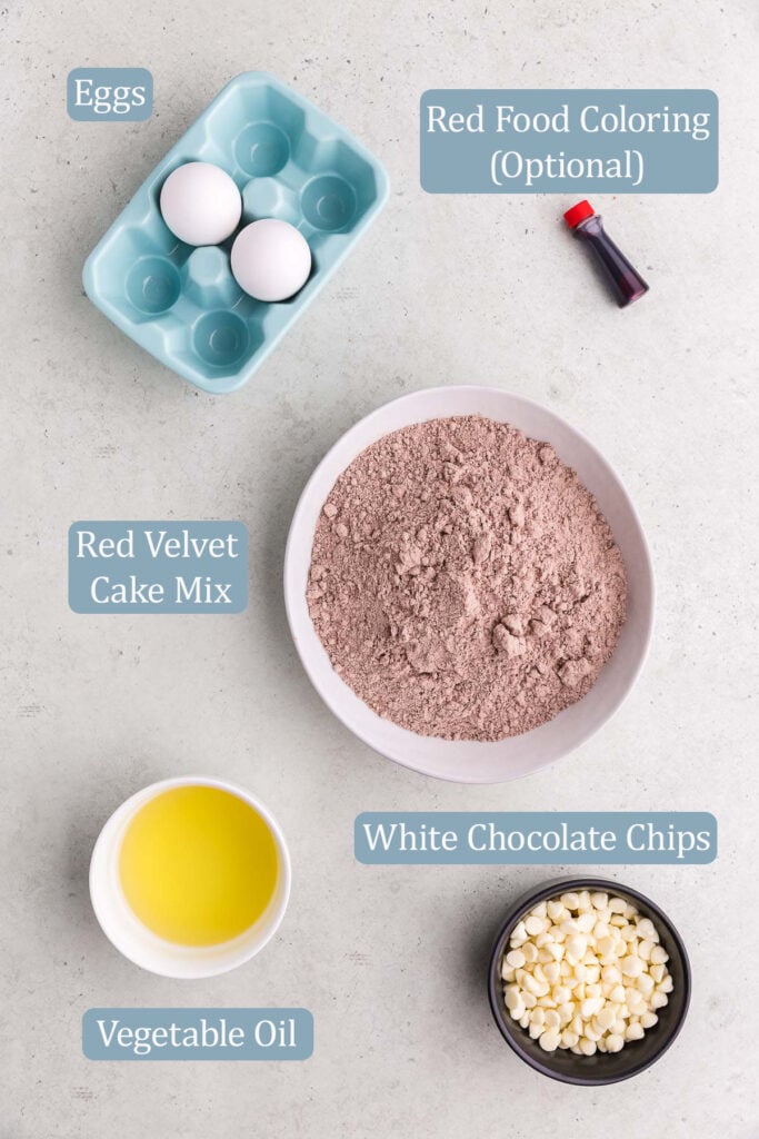 Overhead shot of the ingredients used to make red velvet cake cookies. Ingredients include: eggs, red food coloring (optional), red velvet cake mix, vegetable oil, and white chocolate chips.
