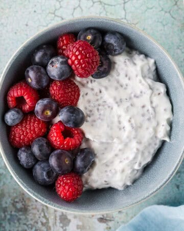 Overhead shot of a high protein Greek Yogurt bowl. Creamy Greek yogurt mixed with chia seeds and topped with fresh blueberries and raspberries.