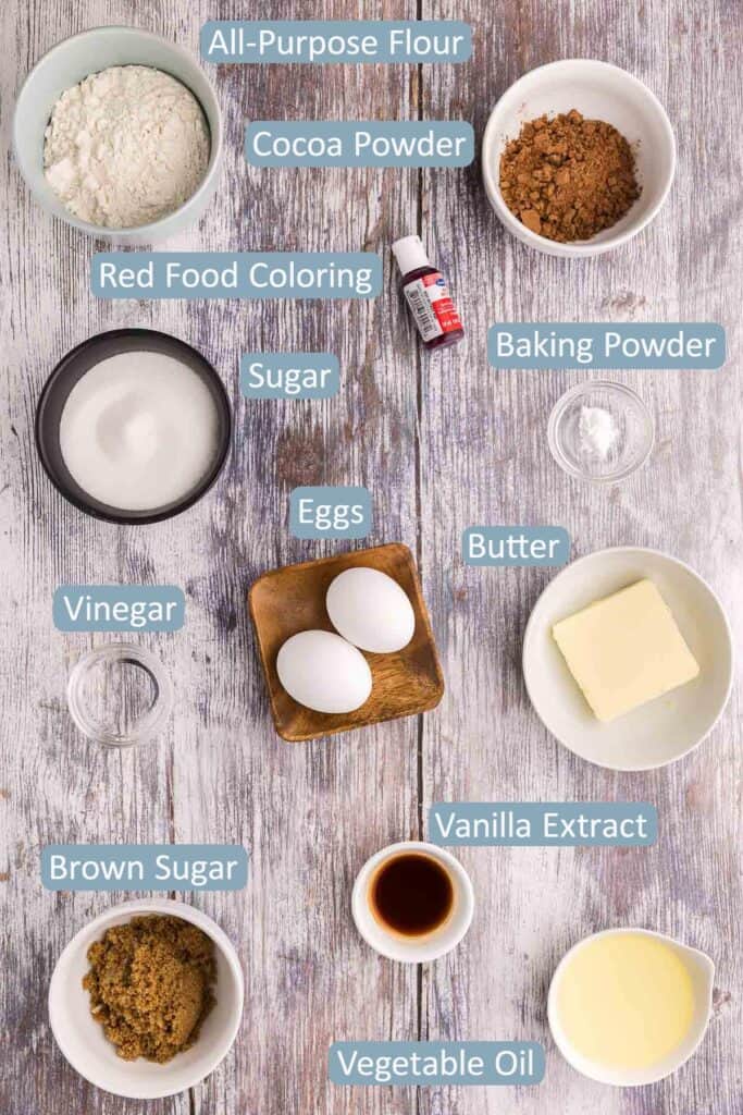 overhead shot of the ingredients used in making red velvet cake brownies.  Ingredients are: flour, cocoa, red food coloring, sugar, brown sugar, baking powder, eggs, butter, vanilla extract, vinegar, and vegetable oil.