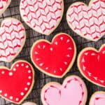 Close up overhead shot of heart-shaped sugar cookies on a cooling rack. The cookies have been decorated in red and pink royal icing.
