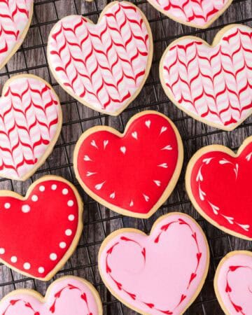 Close up overhead shot of heart-shaped sugar cookies on a cooling rack. The cookies have been decorated in red and pink royal icing.