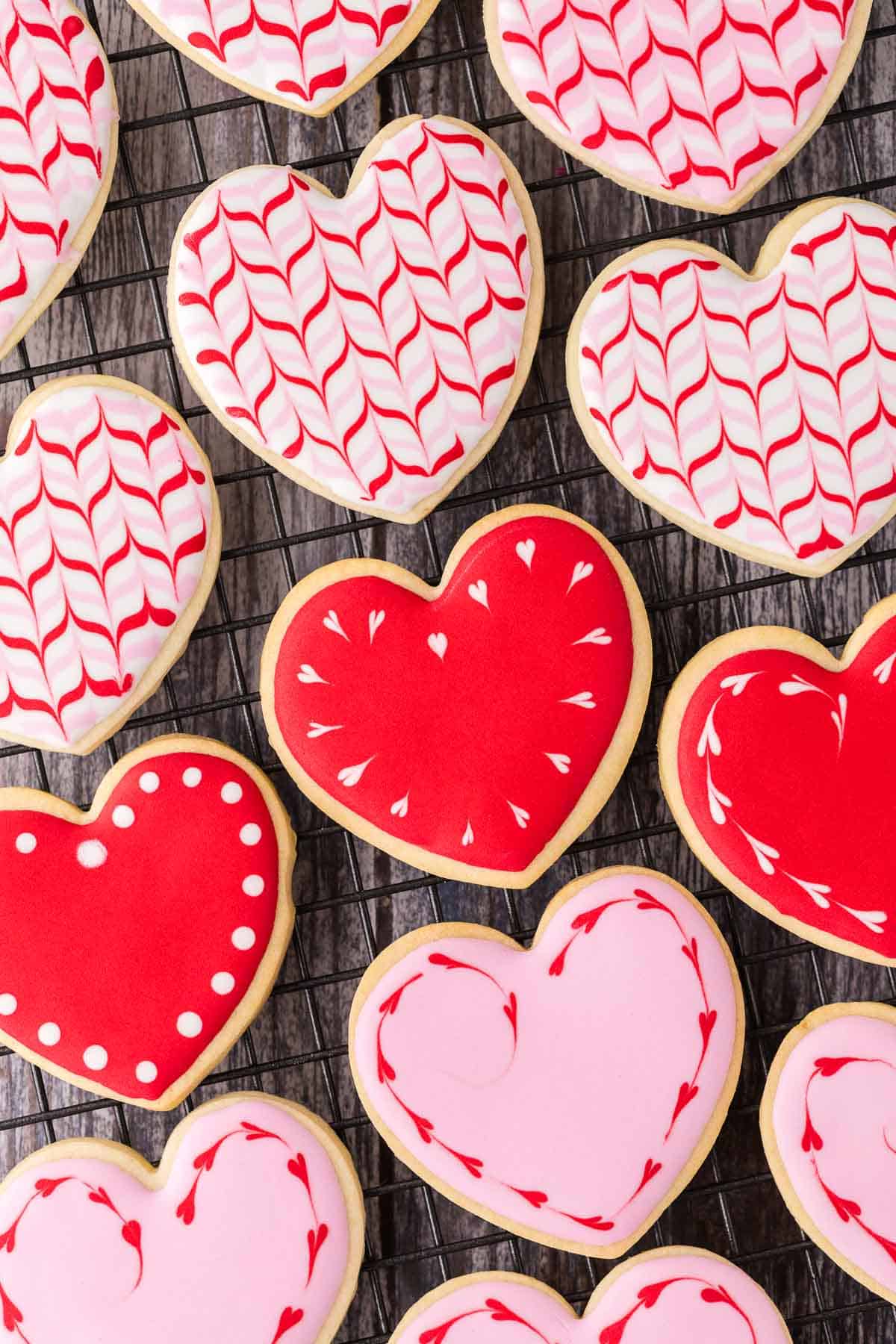 Close up overhead shot of heart-shaped sugar cookies on a cooling rack. The cookies have been decorated in red and pink royal icing.