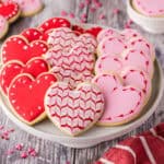 Horizontal low angle shot of a cake platter filled with heart shaped sugar cookies. Each cookie has been decorated with pink or red icing.