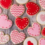 Overhead shot of various heart shaped sugar cookies. All cookies are piped with white, pink, or red royal icing. Some have sprinkles, some have heart-wreaths which have been scribed around the edges.