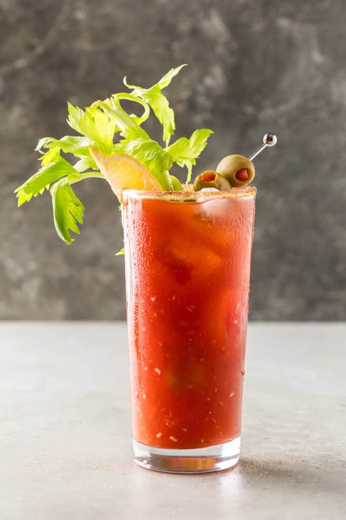 Side shot of a bloody mary drink.  No props just the drink garnished with celery, skewered olives, and a lime wedge.