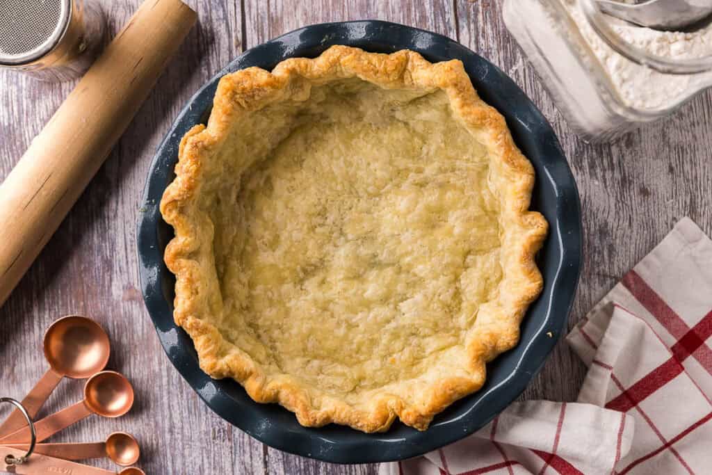 an overhead shot of a par-baked pie shell. It is lightly golden and sits inside a blue pie plate.