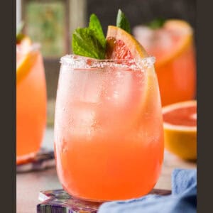 Close up side shot of a paloma drink. This pink cocktail is garnished with a grapefruit wedge and a sprig of mint.