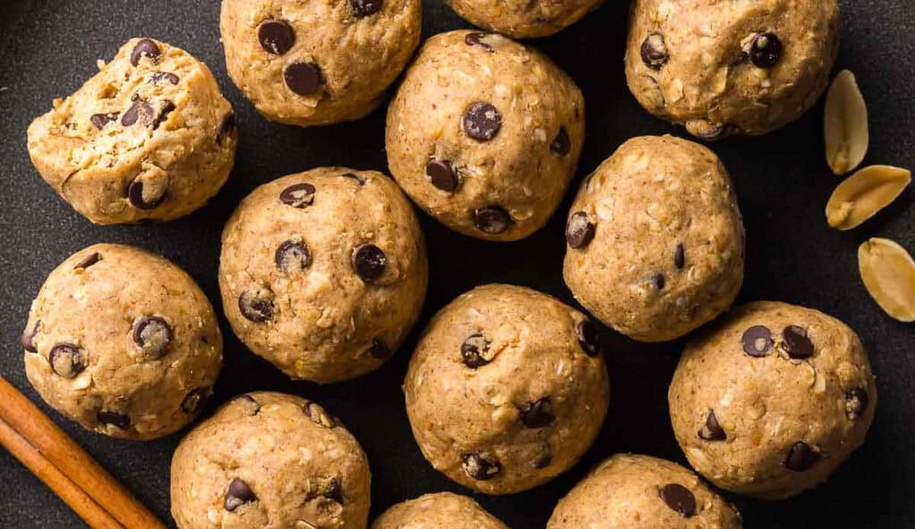 Close up overhead shot of a black plate filled with peanut butter protein balls. The round brown balls all contain mini chocolate chips. One has a bite taken out.