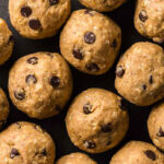 Close up overhead shot of a black plate filled with peanut butter protein balls. The round brown balls all contain mini chocolate chips. One has a bite taken out.
