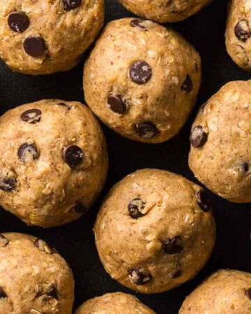 Close up overhead shot of a black plate filled with peanut butter protein balls. The round brown balls all contain mini chocolate chips. One has a bite taken out.