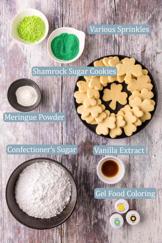 Overhead shot of the ingredients needed to decorate Saint Patty's Day Cookies.  Ingredients are: green colored sprinkles, shamrock shaped sugar cookies, meringue powder, confectioner's sugar, vanilla extract, and gel food coloring.