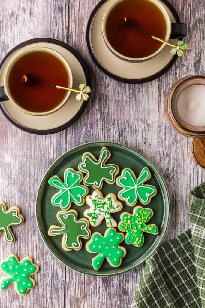 overhead shot of a green plate with green St. Patrick's day sugar cookies with various decorations.  Two teacups are near the top of the photo.