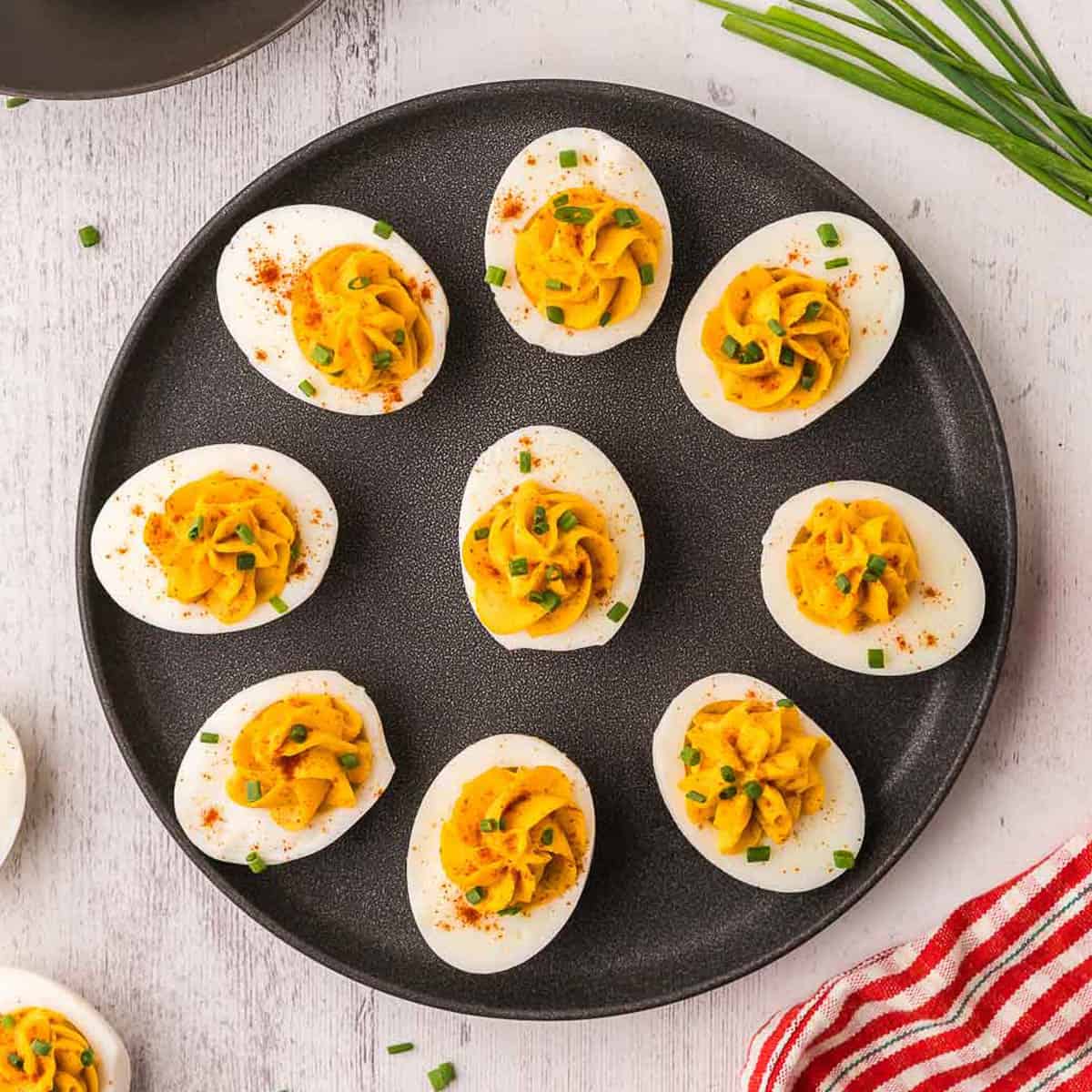 Deviled eggs with mustard, herbs, and spices on black plate.