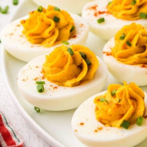 side shot of a serving plate with devilled eggs. Each egg has been nicely piped with the filling and sprinkled with paprika and chopped chives.