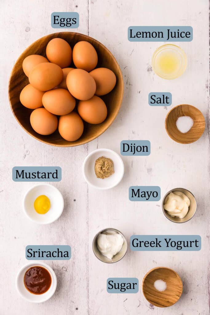 Overhead shot of all the ingredients used in making deviled eggs.  Ingredients are: Eggs, lemon juice, salt, dijon mustard, yellow mustard, mayonnaise, Greek yogurt, sriracha, and sugar.