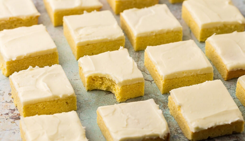 Horizontal shot of lemon cookie bars in neat and tidy rows. One of the middle bars has a bite taken out of it.