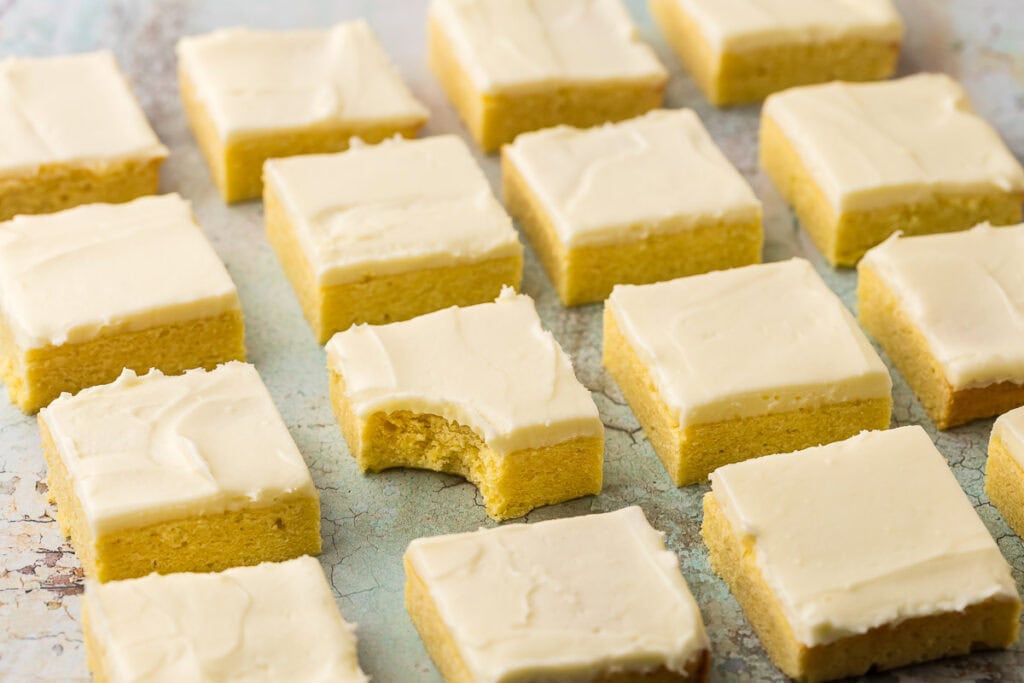 Horizontal shot of lemon cookie bars in neat and tidy rows. One of the middle bars has a bite taken out of it.