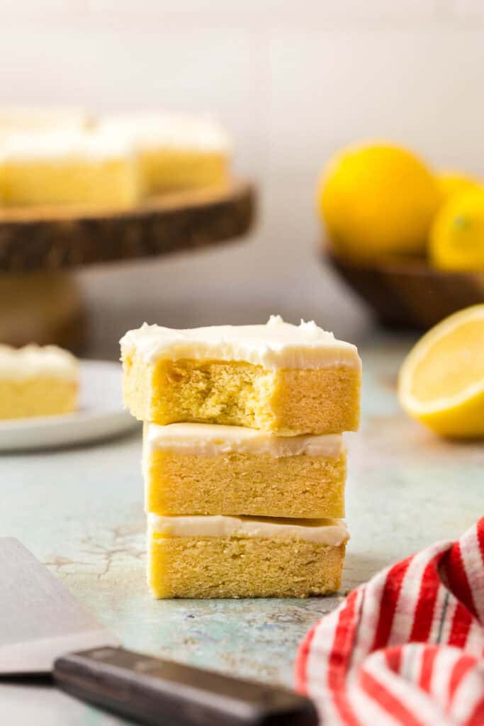 Side shot of a stack of lemon cookie bars with lemon cream cheese frosting. There is a bite out of the top bar.