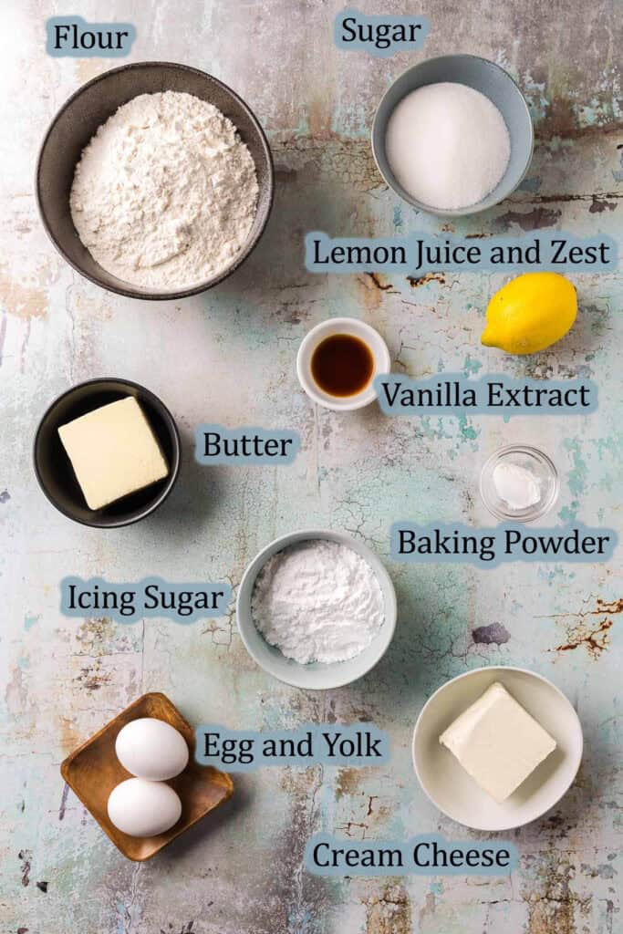 Overhead shot of the ingredients needed to make this lemon cookie bars recipe. Ingredients are: flour, sugar, lemon juice and zest, vanilla extract, butter, cream cheese, baking powder, icing sugar, egg and egg yolk.