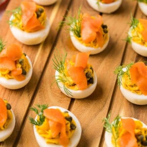 angle shot of smoked salmon devilled eggs lined up on a wooden cutting board.