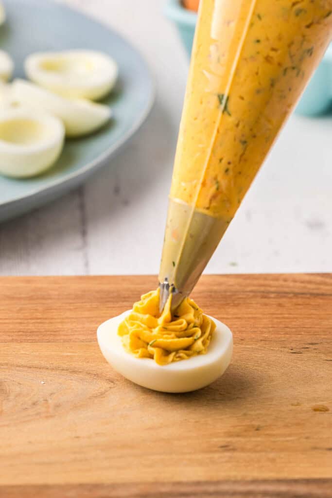 Side shot of a half egg being filled with piped smoked salmon filling.