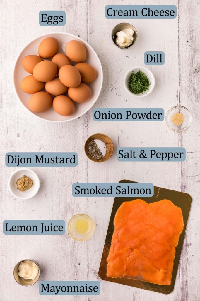 Overhead shot of ingredients used to make smoked salmon devilled eggs. Ingredients include: eggs, smoked salmon, cream cheese, mayonnaise, fresh dill, onion powder, salt and pepper, dijon mustard, and lemon juice.