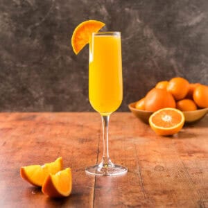 Side shot of a champagne flute filled with yummy orange non-alcoholic mimosa. Garnished elegantly with half an orange wheel.
