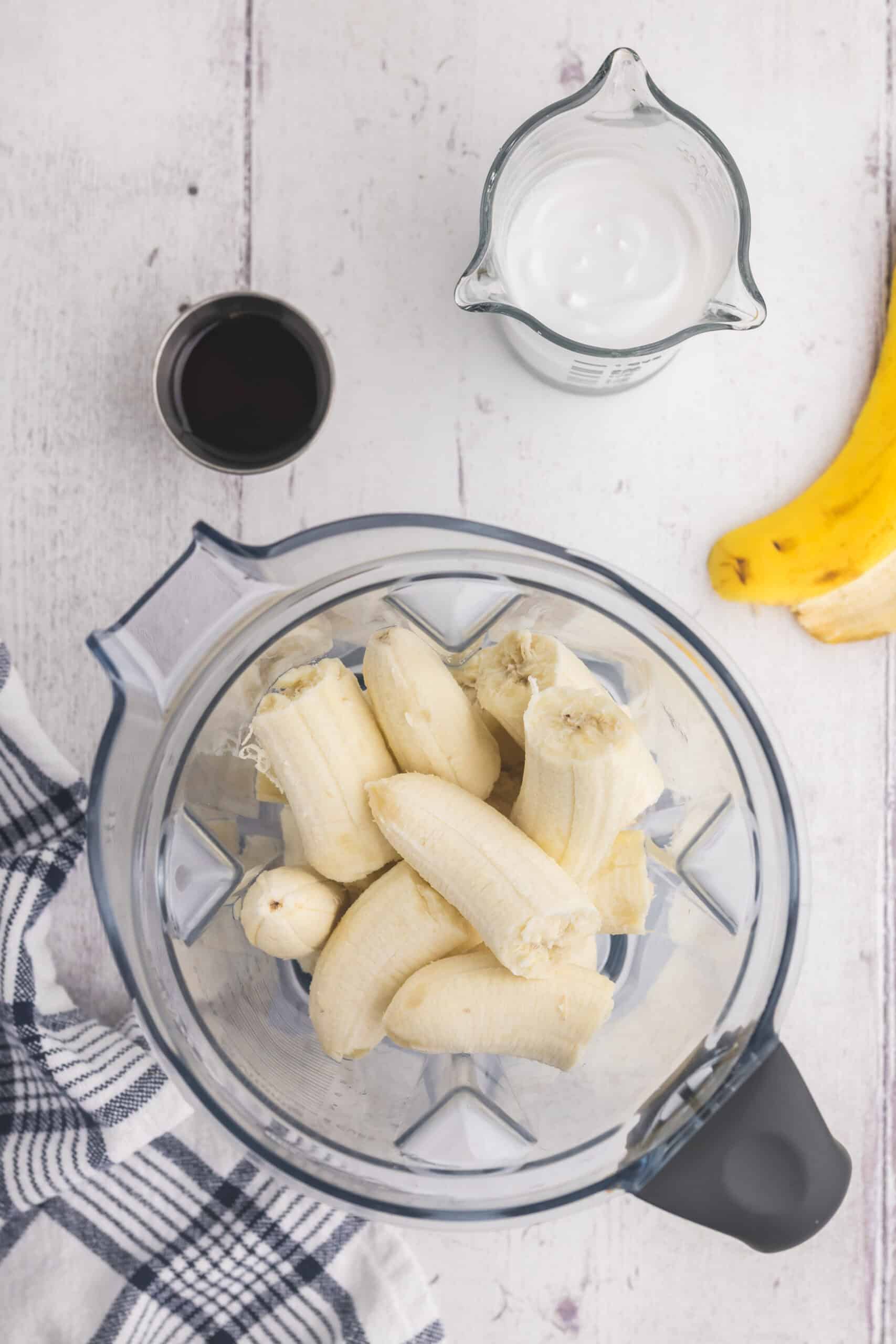 Overhead shot of a blender filled with banana, and above is some coconut milk and maple syrup ready to go in.