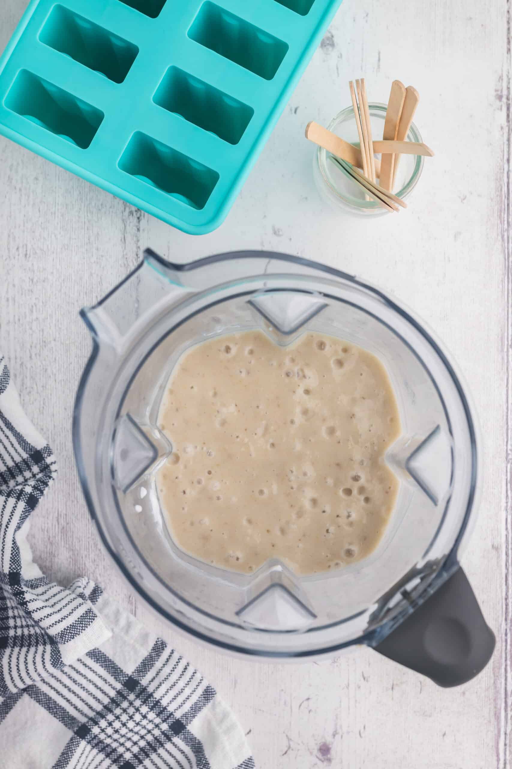 overhead shot of the blender after the bananas, maple syrup, and coconut have been blended together into a creamy beige mixture.