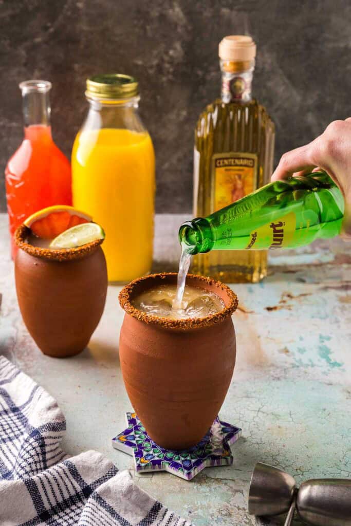 Side shot of a clay cantarito cup being topped off with grapefruit soda.