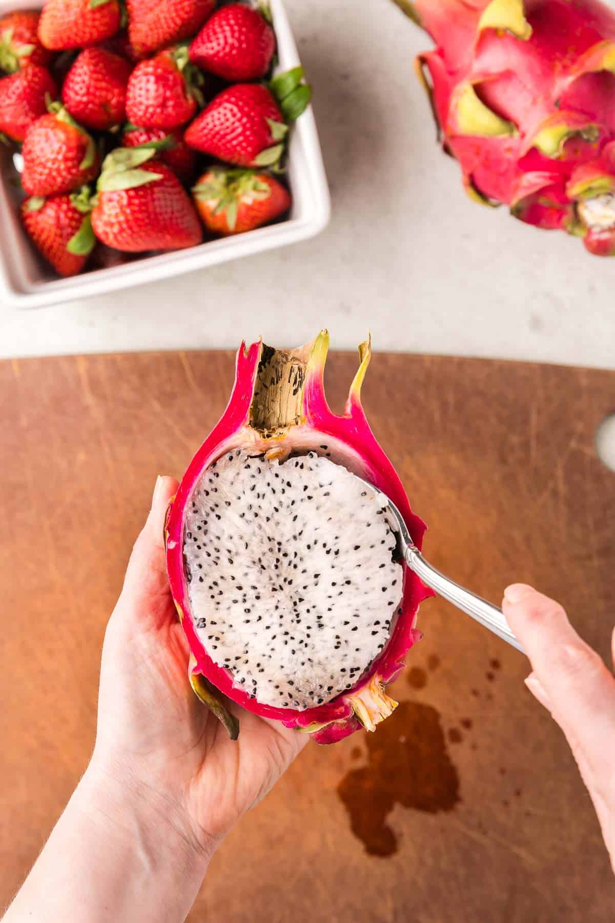 Overhead picture of a sliced dragon fruit with a spoon removing the flesh inside the skin.