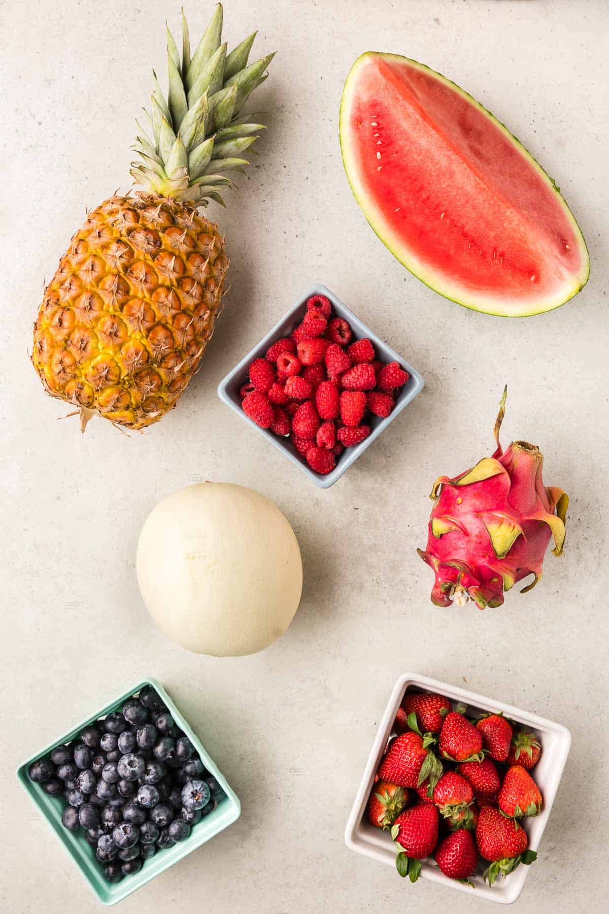 Overhead shot of the ingredients used in making this fruit tray. Ingredients are all fresh: pineapple, watermelon, honeydew, dragon fruit, blueberries, raspberries, and strawberries.