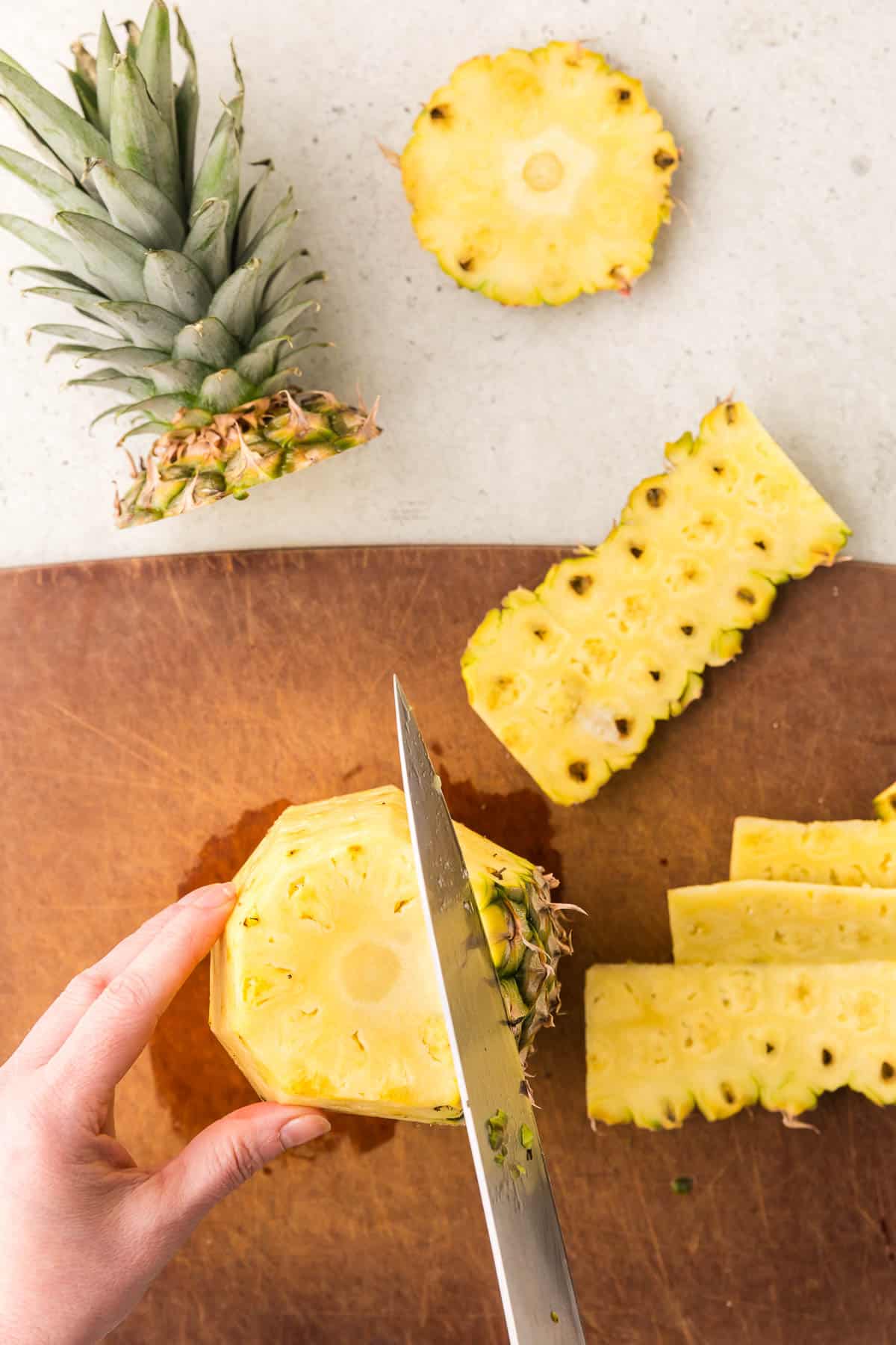 Removing the outside skin from a pineapple. Pineapple is standing vertically while a knife cuts the skin off.