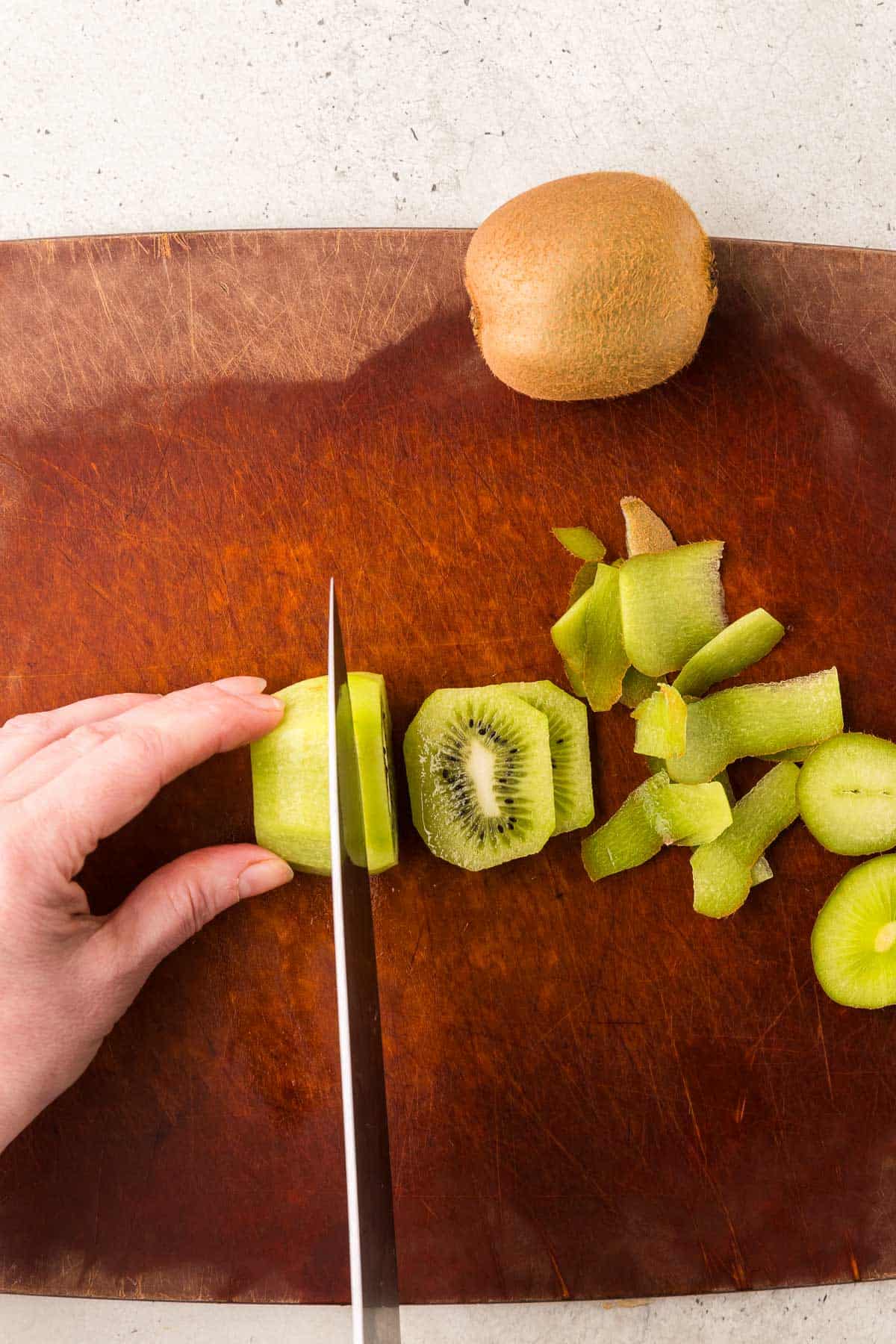 Overhead shot of a kiwi fruit with skin removed being sliced into rounds.