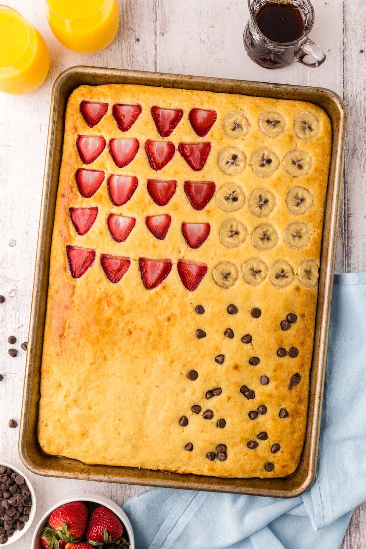 Overhead shot of the sheet pan after it has come out of the oven. The "cake" inside is golden brown and each corner has a different flavor. Top left has strawberries, top right has bananas, bottom left is plain, and bottom right has chocolate chips.