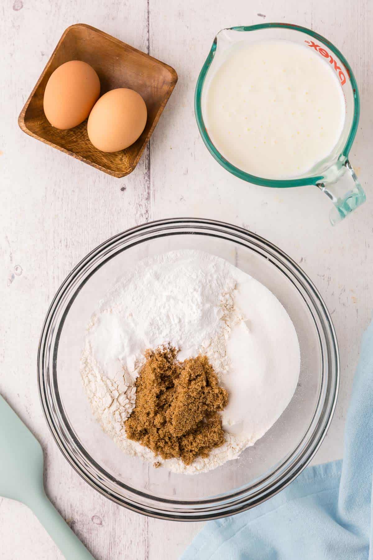 overhead shot of a glass mixing bowl filled with all the dry ingredients, like flour, brown and white sugar, baking powder and baking soda.