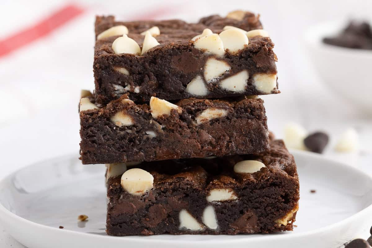 A stack of three chocolate chocolate chip cookie bars. Each one has dark chocolate and white chocolate chips studded in a dark chocolate cookie bar.