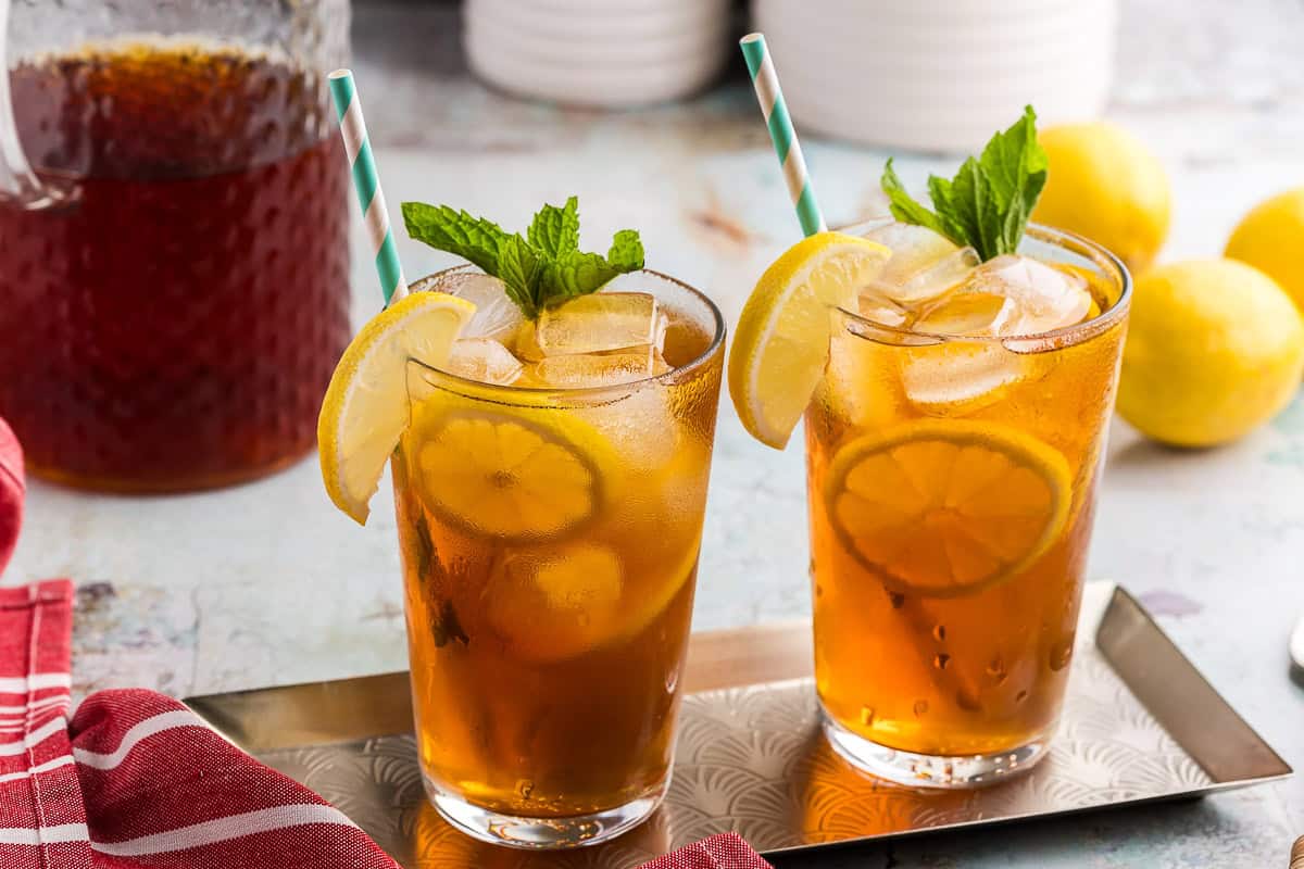 A side shot of two cold brewed iced teas served on a slender metal serving tray. Each glass is filled with ice, cold brew tea, and garnished with lime wheels and wedges and a sprig of mint.