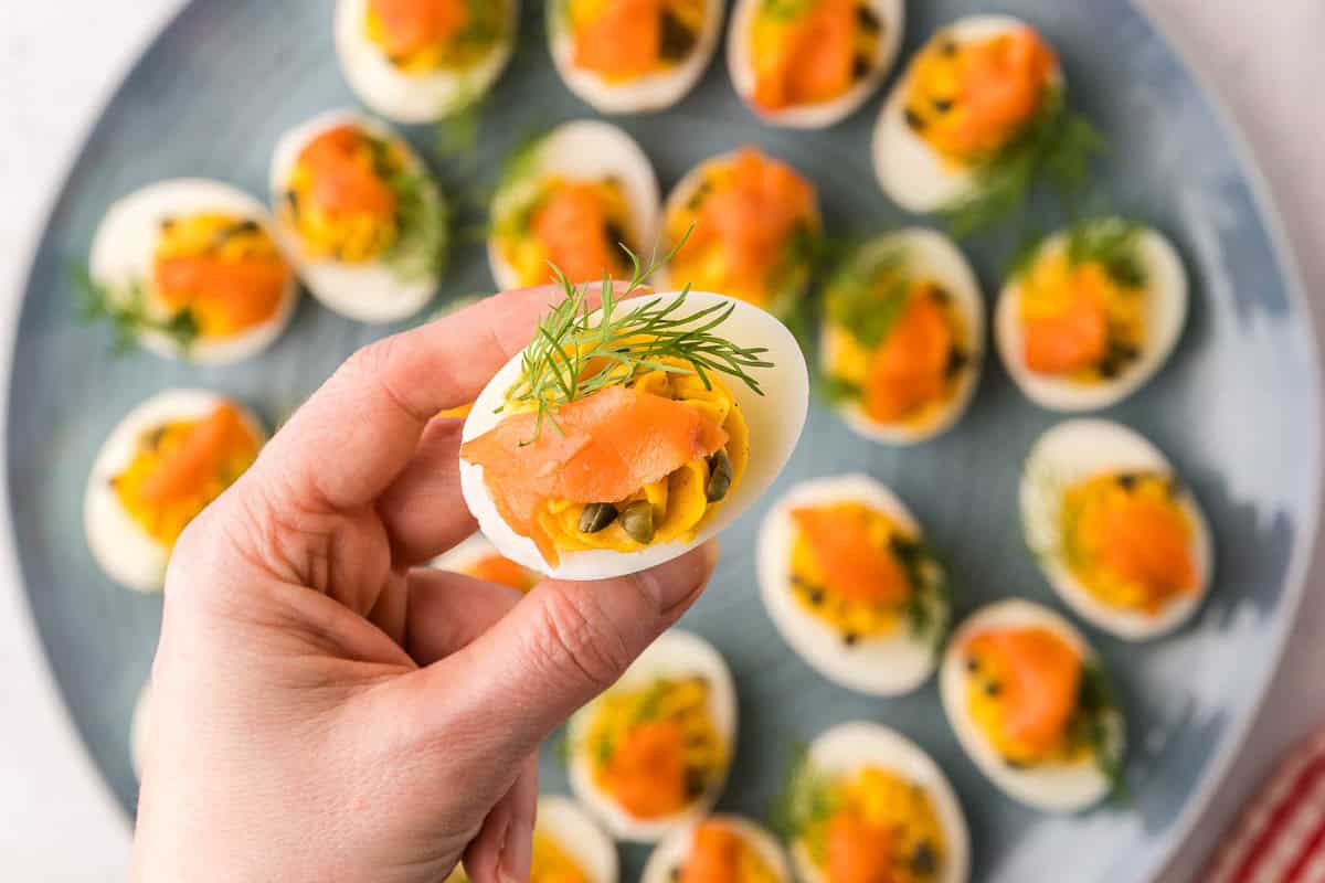 overhead shot of a smoked salmon deviled egg being lifted of a serving platter. The egg is decorated with a sprig of fresh dill and a small piece of smoked salmon.