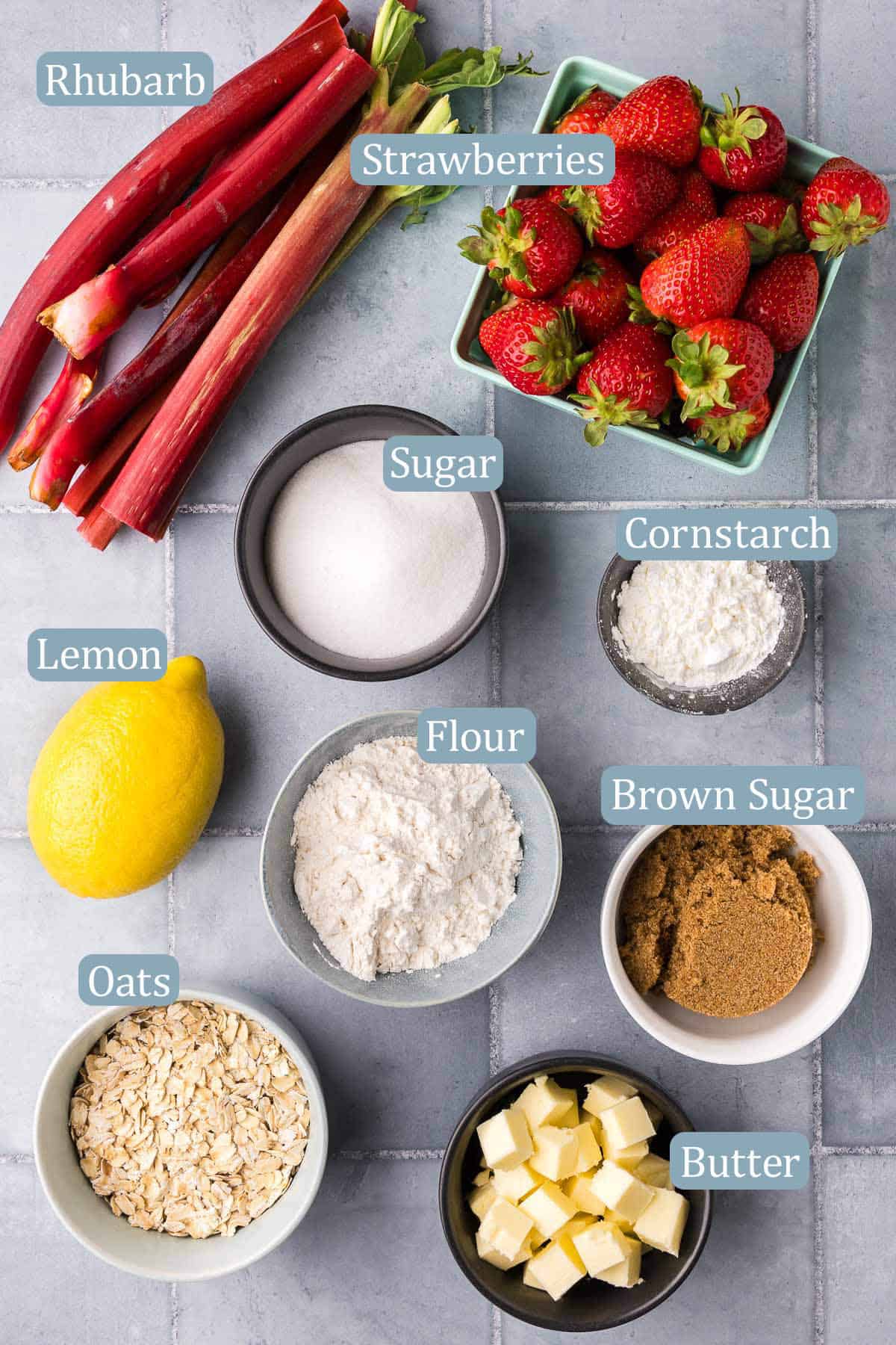Overhead shot of all the ingredients used in making strawberry rhubarb crisp. Ingredients are: rhubarb, strawberries, lemon juice, sugar, cornstarch, flour, brown sugar, oats, and butter.