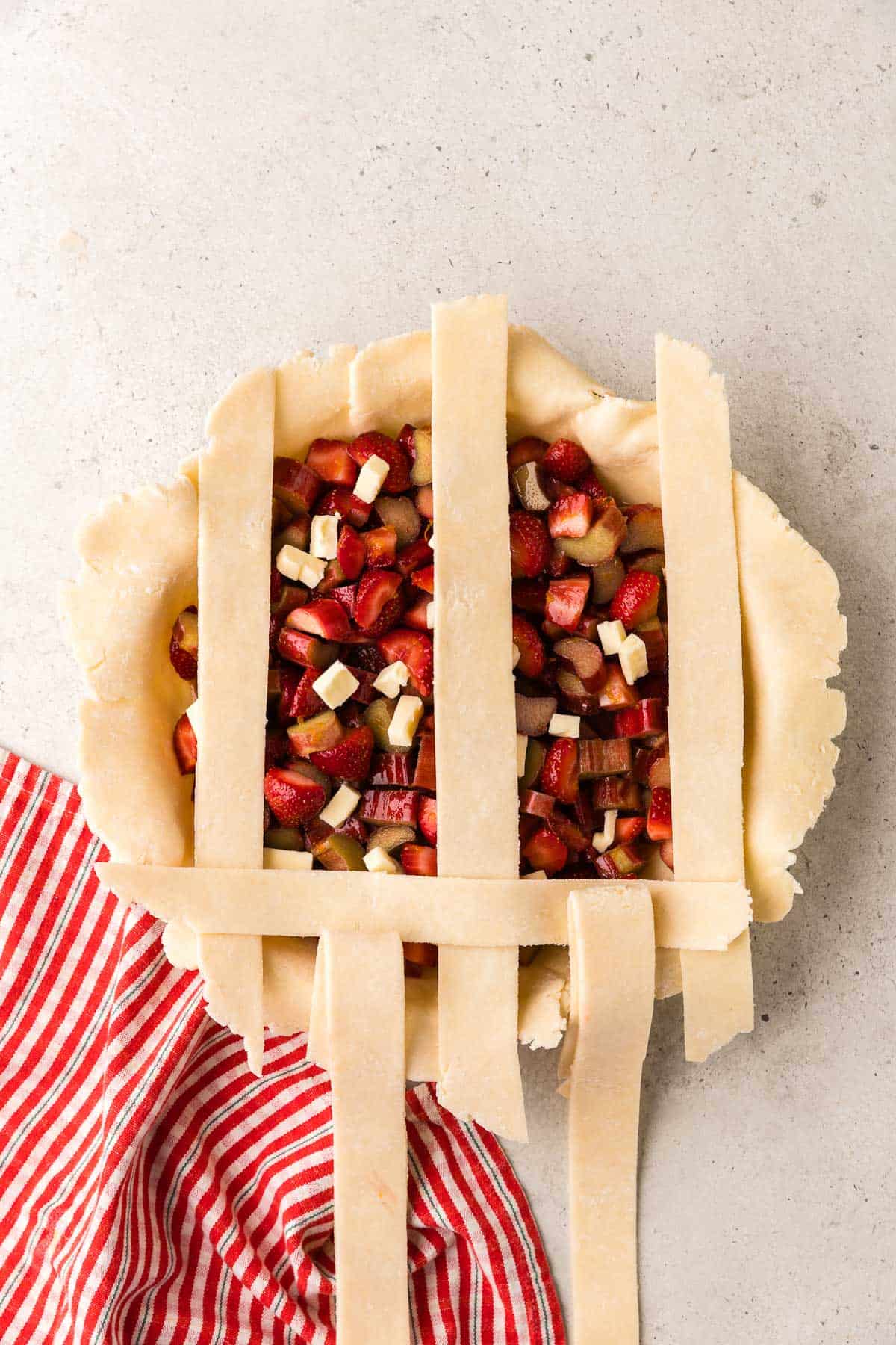 Overhead shot of the strawberry rhubarb pie with every other dough strip pulled back so the lattice top can be started.
