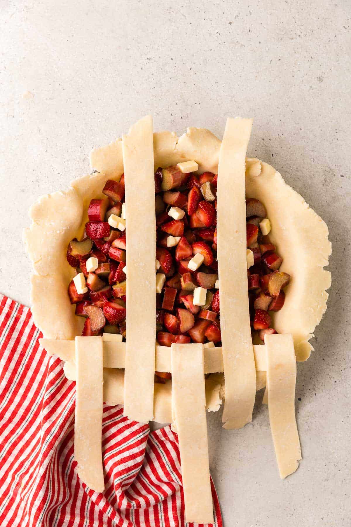 Overhead shot of the strawberry rhubarb pie with one horizontal strip added and the vertical strips returned to their place while the other vertical strips are now folded back.