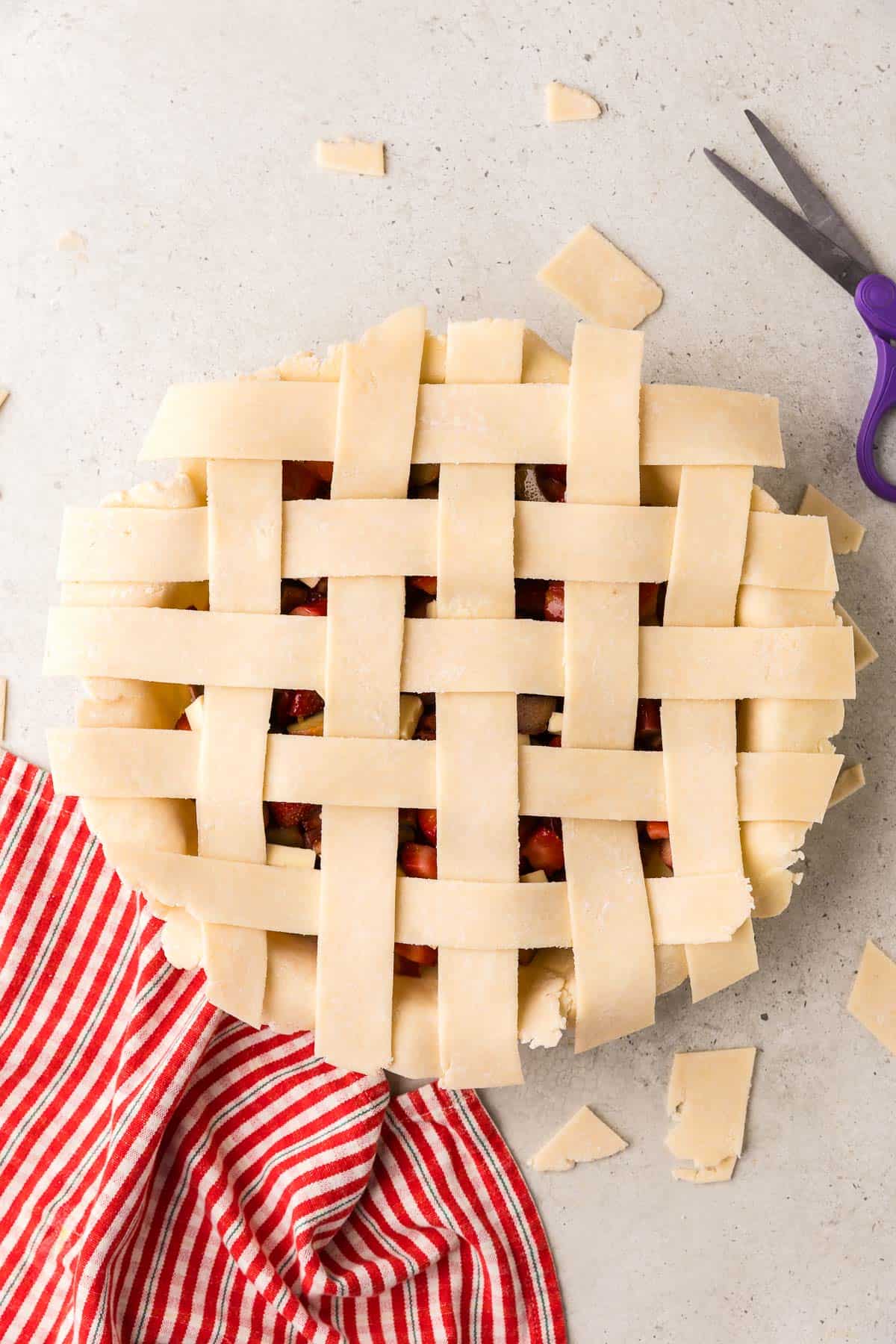 overhead shot of the pie with the top strips forming a lattice top. Scissors have just trimmed the ends of the strips so they are the same length as the bottom pie dough.